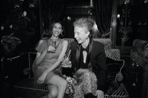 Seated on a zebra-striped sofa, two women drink cocktails and laugh in this black and white image of the saloon