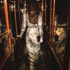 A woman in a silver gown walks along a corridor of highly polished wood and brass fittings towards her private cabin