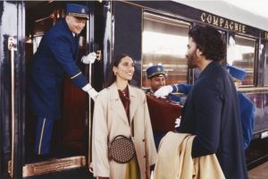 Guests smiling at each other while their luggage is carried onto a luxury train by blue-uniformed stewards